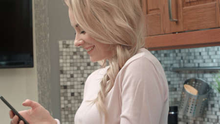 Happy young woman dancing in kitchen listening to music on smartphone and coffee at homeの写真素材