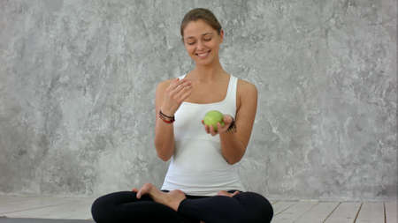 Beautiful smiling woman holding green apple, jungle with it, sitting in lotus poseの写真素材