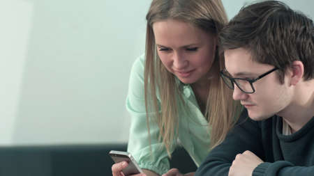 Happy two young students sitting at table and reading text message in libraly in universityの写真素材
