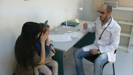Male doctor shaking down thermometer and handing it to little girlの写真素材