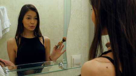 Beauty teenage girl applying make up and admiring herself in the mirrorの写真素材