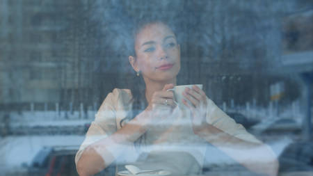 Dreamy young woman with a cup of tea at a cafe watching city lifeの写真素材