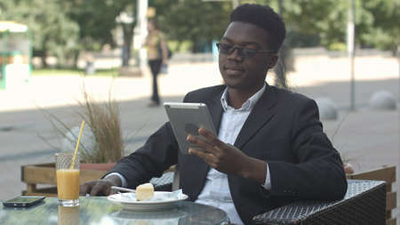 Handsome afro american man is using a tablet, while sitting in outside cafeの写真素材