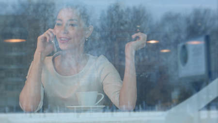 Young woman talking on the phone and playing with her hair in coffee shopの写真素材
