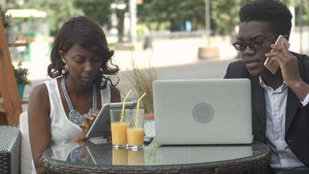 Afro-american business man and woman working together in modern cafe, having phone calls, using laptop and digital tabletの写真素材