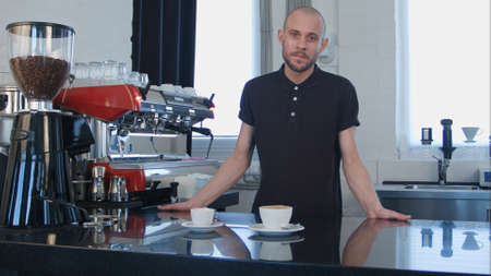 Portrait of a young smiling male barista holding cup of coffee at the cafeの写真素材
