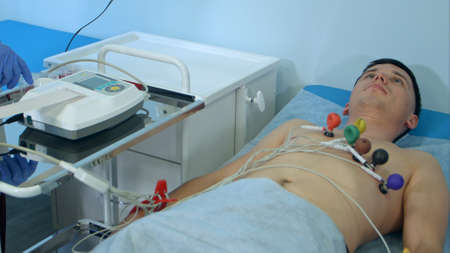 Nurse with ECG equipment making cardiogram test to male patient in hospital clinicの写真素材