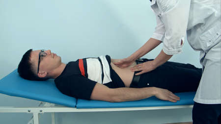 Female doctor examining the abdomen of male patient lying on the hospital sofaの写真素材