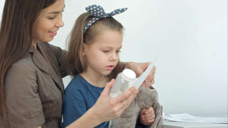 Smiling mother with cute girl holding pills and medical formの写真素材