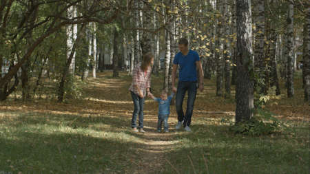 Happy young family is having fun in the autumn park outdoors on a sunny day. Mother, father swing their little baby-boy.の写真素材
