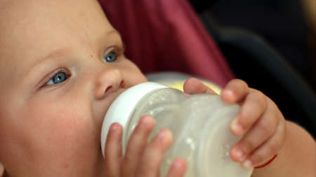 lovely little girl with blue eyes drinking milk from a bottleの写真素材