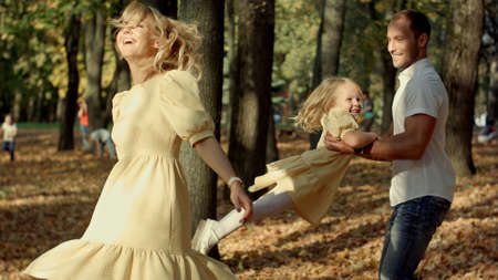 Little girl and her parents playing in the autumn parkの写真素材
