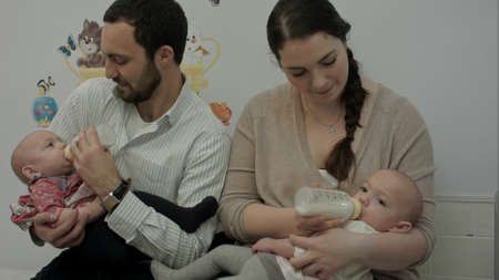 Young couple feed newborn twins from a bottleの写真素材