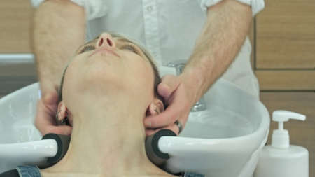 Happy young woman with hairdresser washing head at hair salonの写真素材