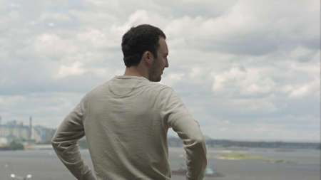 Young man is looking into the distance to the river on a cloudy day.