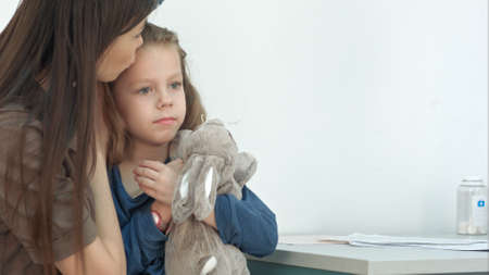 Mother holding little girl and taking her temperature with thermometer at doctor officeの写真素材