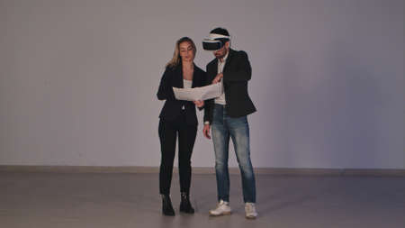 Female architect with building plans discussing construction project with her partner in vr headsetの写真素材