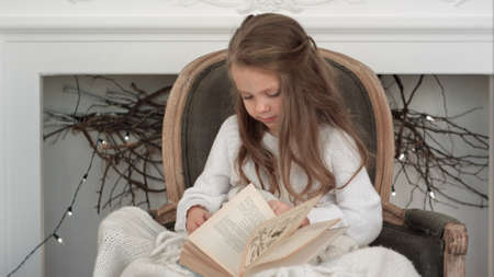 Cute little girl sitting in a Christmas chair and going through a bookの写真素材