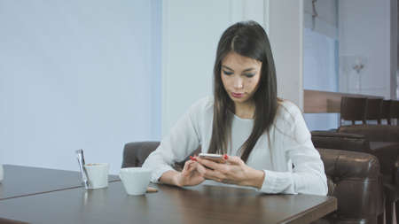 Beautiful young woman texting on smartphone in a cafeの写真素材