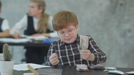 Business boy in eyeglasses counting money, dollars