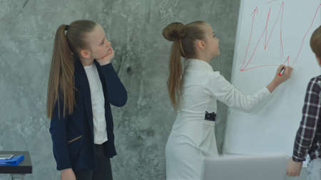 Young business girl drawing on flipchart at office, arguing with little colleaguesの写真素材