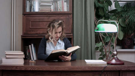 Pretty young female sitting at her desk and researching information in the book for business reportの写真素材