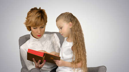 Mother and daughter reading book on the couch on white backgroundの写真素材