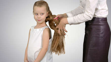 Mother makes daughter hairstyle on white backgroundの写真素材