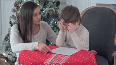 Young mother helping her struggling son to write a letter to Santa Clausの写真素材