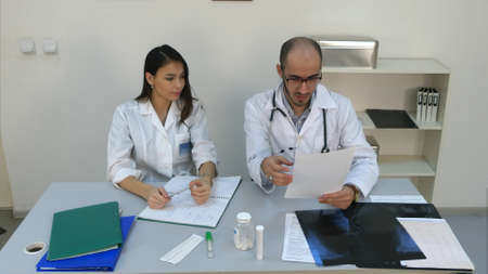 Doctor showing his female assistant how to read cardiogram while she making notesの写真素材