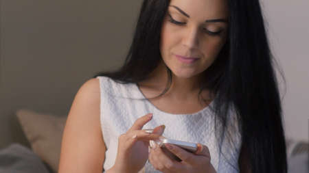 Worried woman sitting on sofa and texting on smartphone at nightの写真素材