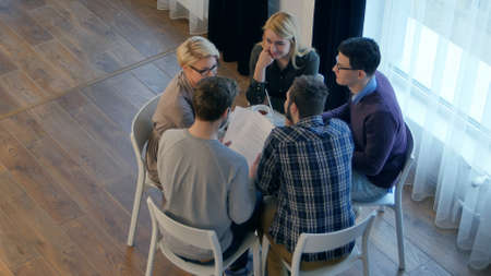 Team communication, group of five people discussing something with smile while sitting at the office tableの写真素材