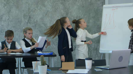 Kids working hard in office, discussing serious problems together, using flipchartの写真素材