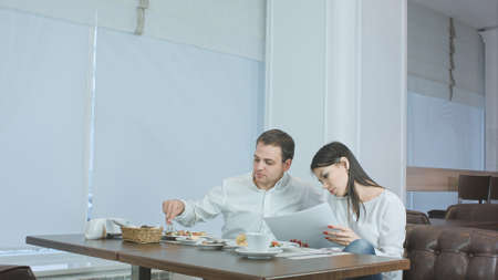 Young female talking on the phone during lunch and asking her male coworker for helpの写真素材