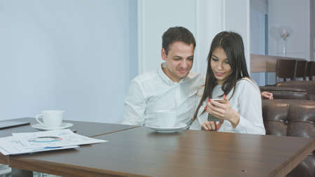 Two office coworkers in a cafe looking at their photos on the phone and laughingの写真素材