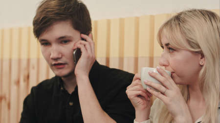 Couple sitting in cafeteria, man calling by mobile phone, woman drinking coffeeの写真素材