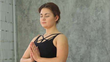 Portrait of young beautiful athletic girl practicing indoor yoga with closed eyes and palms in namaste gestureの写真素材