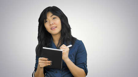 Cheerful attractive asian girl listening and writing down notes on white backgroundの写真素材