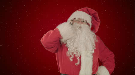 Santa talking on his cellphone with a surprised look on his face. on red background with snowの写真素材
