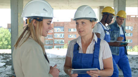Female engineer and worker on construction site with plan on digital tabletの写真素材
