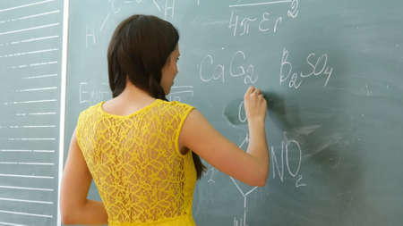 pretty young female college student writing on the chalkboard blackboard during a chemistry classの写真素材
