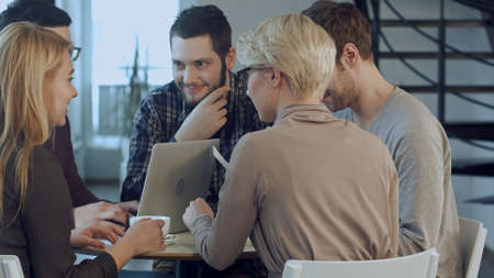 Group of five people discussing something with smile while sitting at the office tableの写真素材