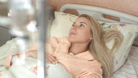 Young woman looks at infusion bottle on the stand in the hospital