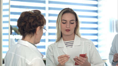 Older nurse bringing medical document to young nurse and male doctorの写真素材