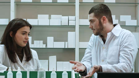 Two adult pharmacists having conflict, discussing problems at pharmacyの写真素材