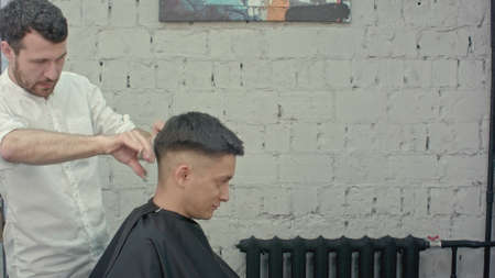 Great time at barbershop. Cheerful young bearded man getting haircut by hairdresserの写真素材