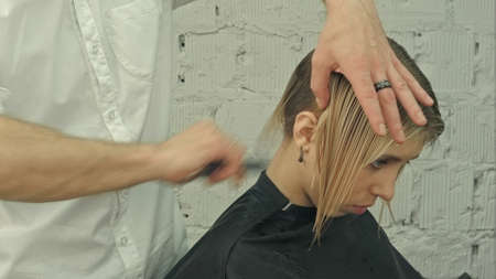 Smiling client sitting in a hair salon while hairdresser is combing her hair. Focus on clientの写真素材