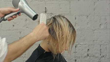 Hairdresser blowing with hairdryer womans hair at the beauty salonの写真素材