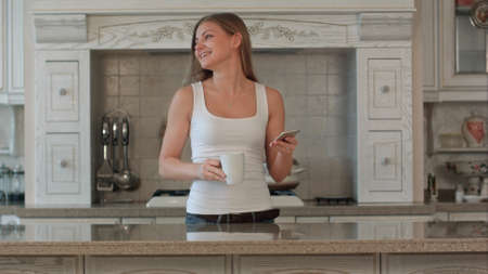 beautiful happy young woman with phone drinking coffee at homeの写真素材