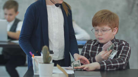 Little businessman holding money and giving salary in officeの写真素材